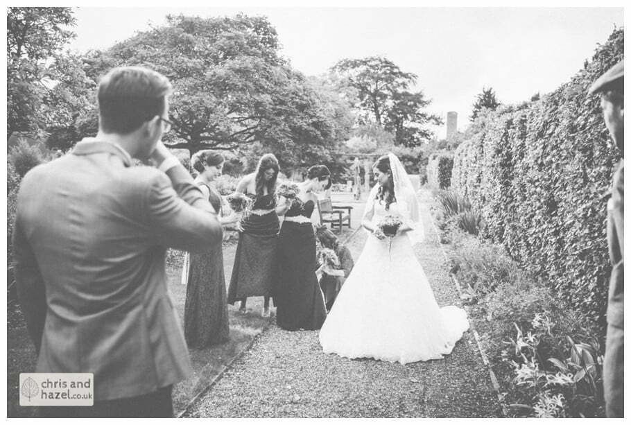 bride walking through gardens to wedding ceremony in greenhouse conservatory documentary Hull Wedding Photographer Bishop Burton College Wedding Photography Hull by Chris and Hazel Wedding Photography Ross laurelin Matulis