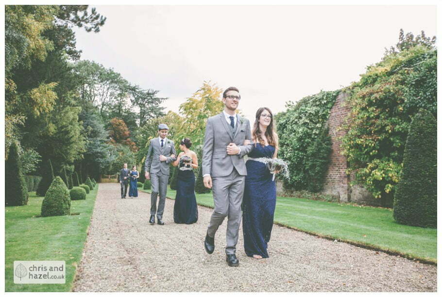 bridesmaid walking with groomsmen down aisle wedding ceremony in greenhouse conservatory documentary Hull Wedding Photographer Bishop Burton College Wedding Photography Hull by Chris and Hazel Wedding Photography Ross laurelin Matulis