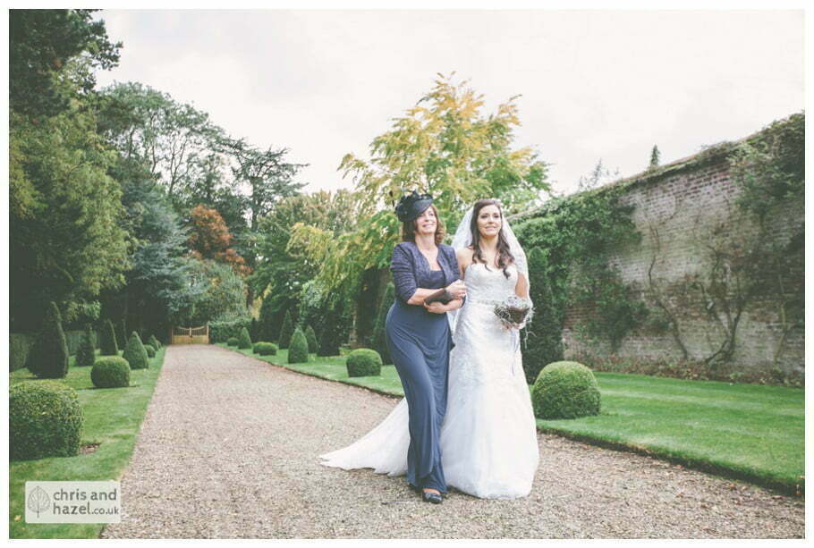 bride walking with mother of bride down aisle wedding ceremony in greenhouse conservatory documentary Hull Wedding Photographer Bishop Burton College Wedding Photography Hull by Chris and Hazel Wedding Photography Ross laurelin Matulis